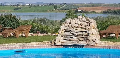 a swimming pool with a stone wall next to a lake at Hacienda El Santiscal in Arcos de la Frontera