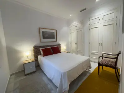 a bedroom with a white bed with two lamps and a chair at Las Marinas de la Bahia in Cádiz