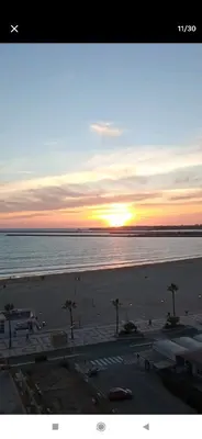 a sunset over a beach with palm trees and the ocean at Valdelagrana vista al mar Puerto de Santa María in El Puerto de Santa María