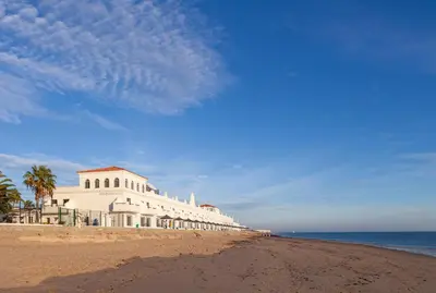 a white building on a beach with the ocean at Playa de la Luz in Rota