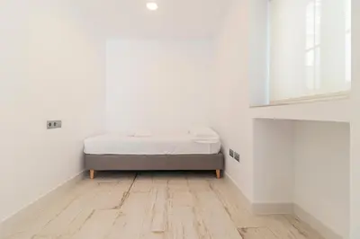 a bed in a white room with a wooden floor at Allo Apartments San Roque 3ºA in Cádiz