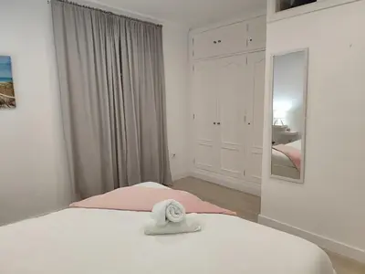 a white bedroom with a bed and a mirror at Apartamento Catamarán in El Puerto de Santa María