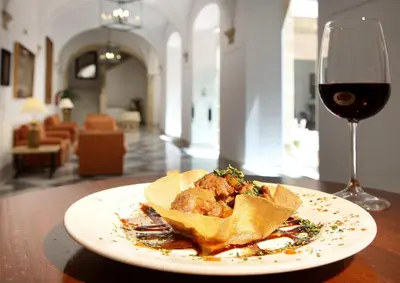 a plate of food next to a glass of wine at Crisol Monasterio de San Miguel in El Puerto de Santa María
