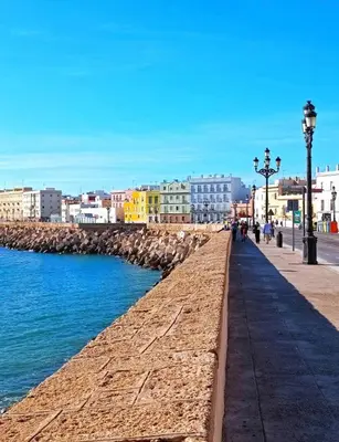 a sidewalk next to the ocean with buildings and street lights at Botánico Playa y Ascensor Grupo AC Gestion in Cádiz