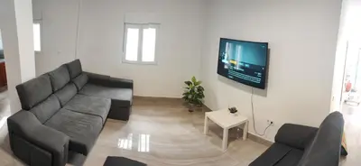 a living room with a couch and a tv on a wall at Precioso bajo muy grande a 200 metros de playa in Chipiona