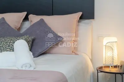 a bed with pink and grey pillows and a lamp at Apartamento El Mirador del Paso (Feel Cádiz) in Cádiz