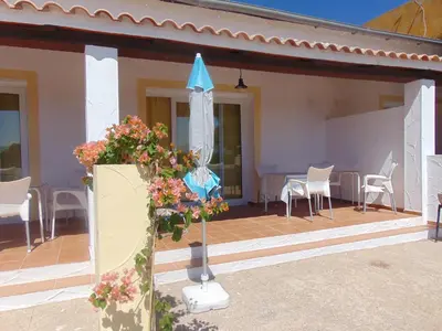 a patio with chairs and an umbrella and some flowers at Studio andalou , campagne , chevaux , piscine commune in Arcos de la Frontera