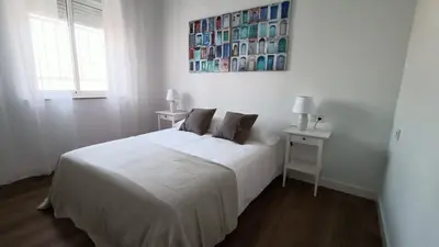 a white bedroom with a bed and a painting on the wall at Apartamento Victoria in Cádiz
