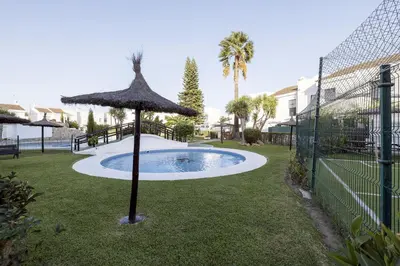 a pool with an umbrella and a fence at Duplex Near the Beach in Chiclana de la Frontera