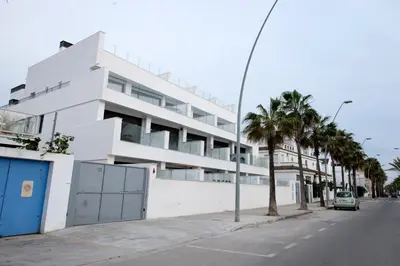 a white building on the side of a street with palm trees at Arenas de Sanlúcar in Sanlúcar de Barrameda