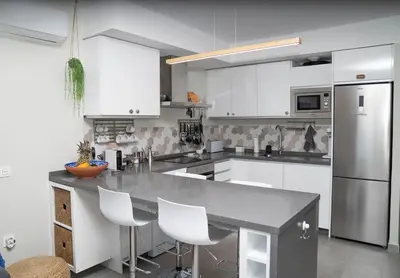 a kitchen with white cabinets and a counter with white chairs at Arenas de Sanlúcar in Sanlúcar de Barrameda