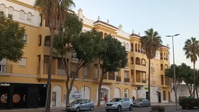 a yellow building with cars parked in front of it at Apto MANAMAR - Entre centro y playa - Parking privado gratis in Sanlúcar de Barrameda
