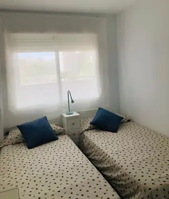 two beds with blue pillows in a small bedroom at Sanlúcar Playa de las Piletas in Sanlúcar de Barrameda