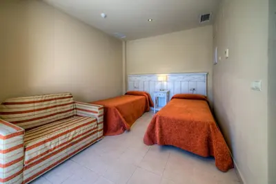 a room with two beds and a chair in it at Apartamentos Piedramar in Conil de la Frontera