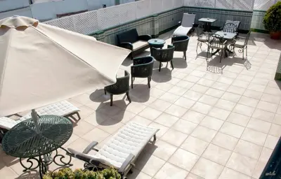 an outdoor patio with chairs and tables and an umbrella at Apartamentos Turísticos Los Patios in Rota