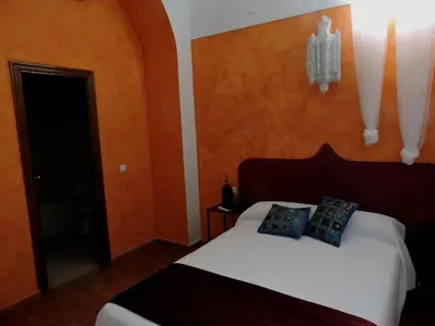 a bedroom with a bed with white sheets and orange walls at Hotel La Fonda del Califa in Arcos de la Frontera