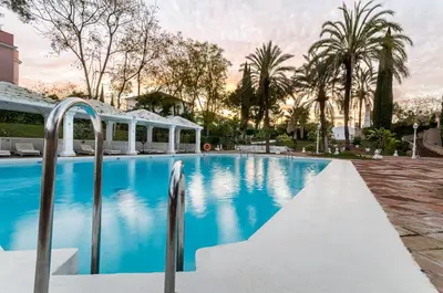 a swimming pool with blue water and palm trees at Exe Guadalete in Jerez de la Frontera