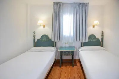 two beds in a room with a table and a window at Apartamentos Soho Boutique Vistahermosa in El Puerto de Santa María
