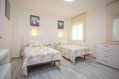 two beds in a bedroom with white walls and wooden floors at Wehost-costaluz Apartamento Sanlúcar con parking in Sanlúcar de Barrameda