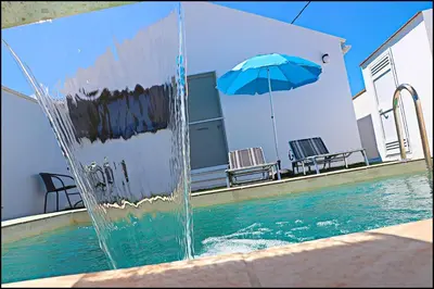 a fountain in front of a swimming pool with a blue umbrella at Chalet los Morenos in Conil de la Frontera