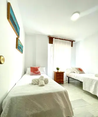 a white bedroom with two beds and a window at GATU Villa Sol, junto a la playa , piscina, 2 baños, aire cc, terraza, 