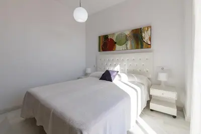 a white bedroom with a white bed and a painting at Atico Costa Doñana in Bonanza