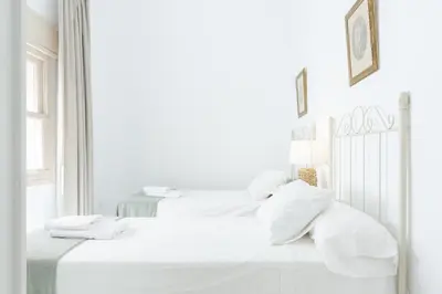 two beds in a white bedroom with white sheets and pillows at Apartamento independiente en Playa de Regla. in Chipiona