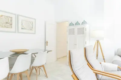a white dining room with white chairs and a table at Amplio apartamento en Playa de Regla. 2. in Chipiona