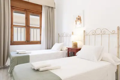 two beds in a white room with a window at Amplio apartamento en Playa de Regla. 2. in Chipiona