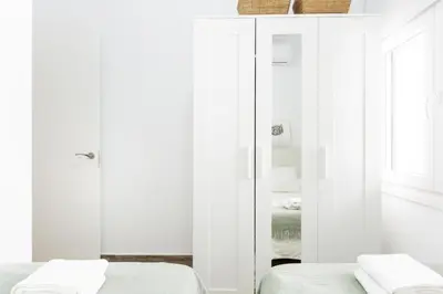 a white bedroom with two beds and a mirror at Precioso apartamento con Chimenea patio solarium. in Chipiona