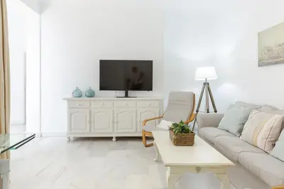 a white living room with a couch and a tv at Luminoso y amplio piso en Chipiona. 5. in Chipiona