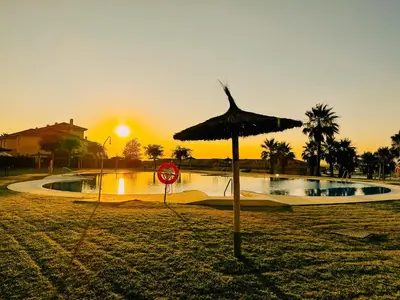 an umbrella in the sand next to a swimming pool at Mika's House Lite in Sanlúcar de Barrameda