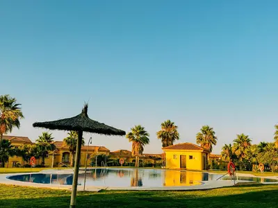 a large swimming pool with an umbrella next to a house at Mika's House Lite in Sanlúcar de Barrameda