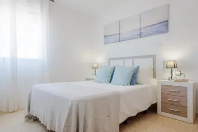a white bedroom with a large bed with blue pillows at La Barrosa con vistas al mar in Novo Sancti Petri