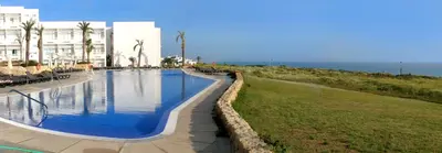 a large swimming pool next to a building and the ocean at Garbí Costa Luz in Conil de la Frontera