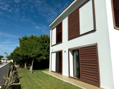a white house with brown shutters on the side of it at Villa Los Pinares de Monaco en Roche, Conil, Cádiz in Conil de la Frontera