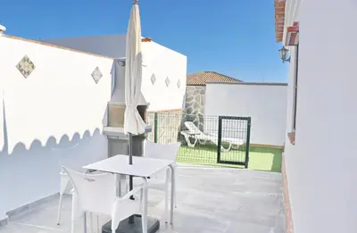 a patio with white chairs and a table and an umbrella at Chalet La Higuerita in Conil de la Frontera