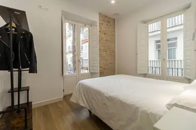 a white bedroom with a bed and two windows at Apartamentos La Cruz Verde in Cádiz