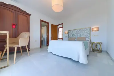 a white bedroom with a bed and a chair at Hotel El Convento in Arcos de la Frontera