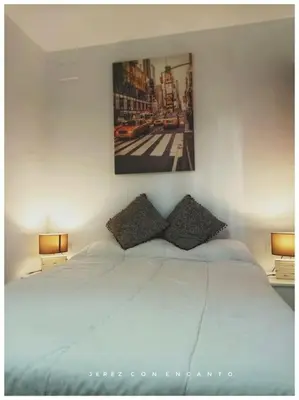 a white bed with two pillows and a picture on the wall at Ático en pleno centro de Jerez sin ascensor in Jerez de la Frontera