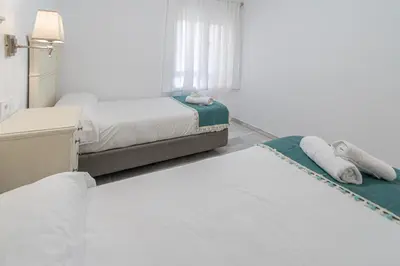 a white bedroom with two beds and a mirror at Apartamento El parador del boticario in Cádiz