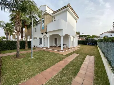a white house with palm trees in a yard at Casa Rosa in Chiclana de la Frontera