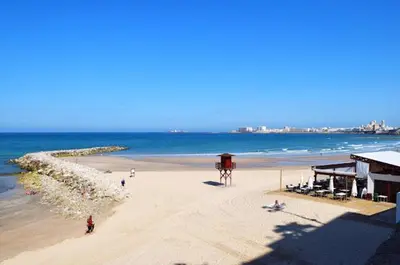 a beach with people and a building and the ocean at Apartamento Cádiz Costa in Cádiz
