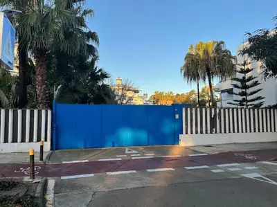a blue fence next to a street with palm trees at Apartamento en Costa Ballena, Urb. Playa Ballena in Cádiz