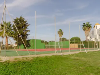 a tennis court with a net and some palm trees at Aparta-club la Barrosa 116 in Chiclana de la Frontera