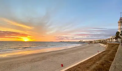 a beach with a lighthouse and the ocean at sunset at 50m Playa Caleta y Teatro Falla Grupo AC Gestion in Cádiz