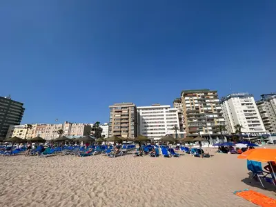 a sandy beach with chairs and umbrellas and buildings at Ático primera línea de playa. in Cádiz