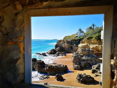 a window view of a beach with rocks and the ocean at CÁDIZ - BUDA, acogedor apartamento en Chiclana de la Frontera, España in Chiclana de la Frontera