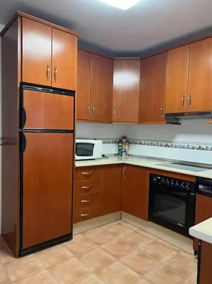 a kitchen with wooden cabinets and a black refrigerator at Casa duplex en chipiona in Chipiona