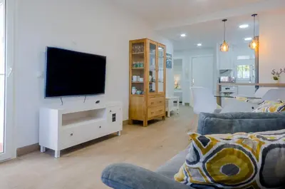 a living room with a couch and a television on a white cabinet at Laja Bermeja, piscina y primera línea de La Barrosa in Chiclana de la Frontera